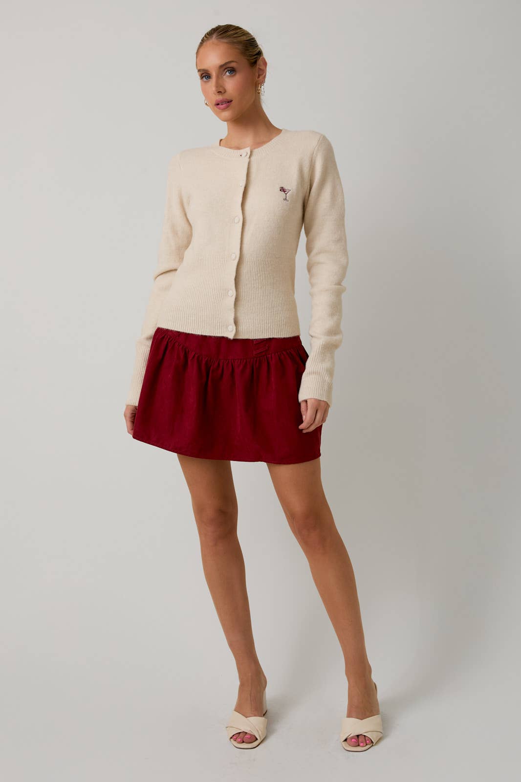 Woman wearing a cream cardigan and red skirt on a white background