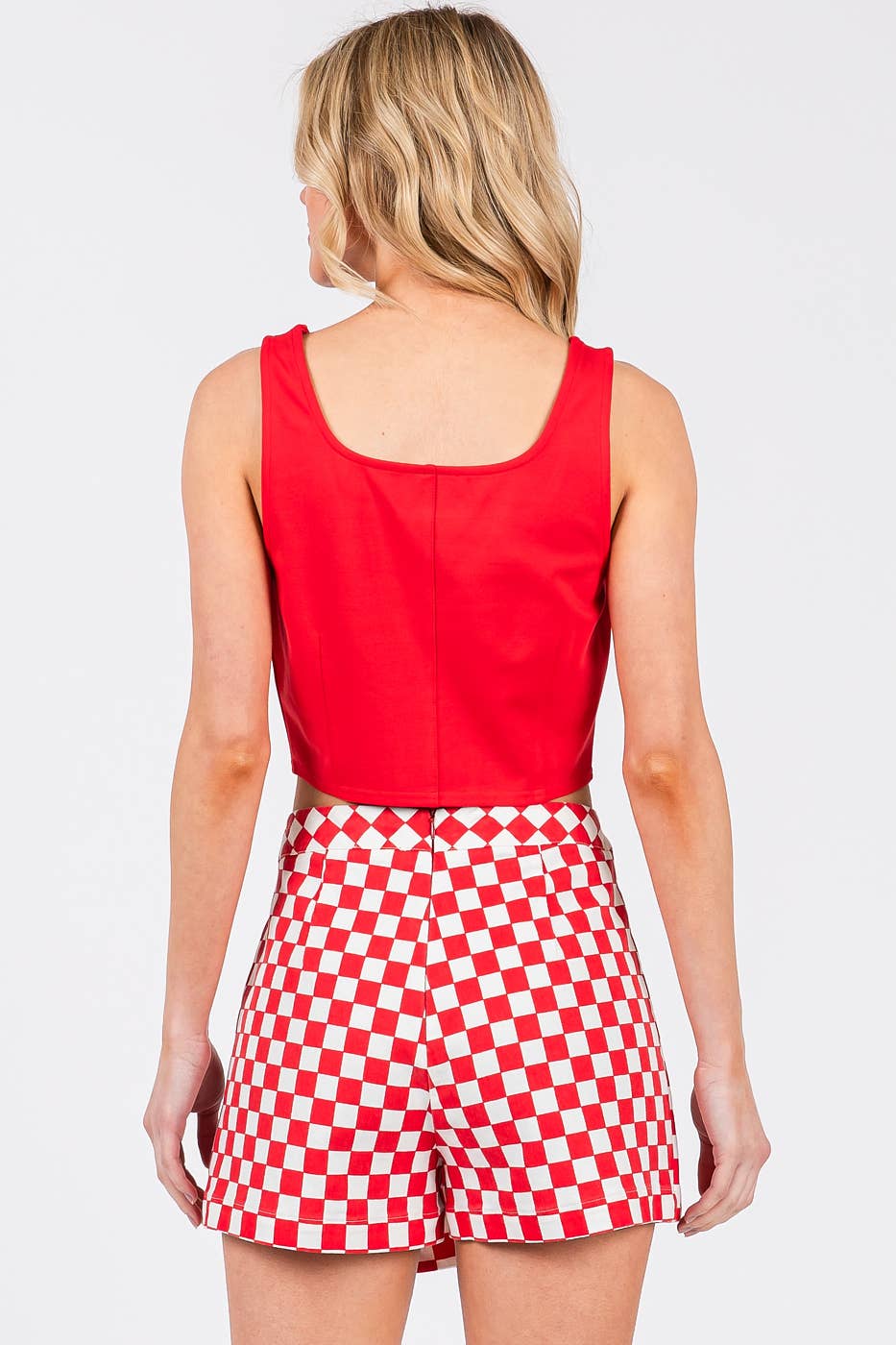 Person wearing a red sleeveless top and red and white checkered shorts on a light gray background