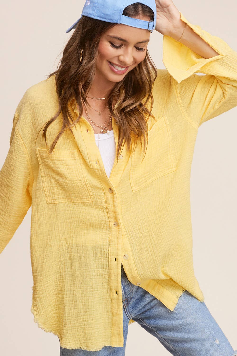 Woman wearing a yellow shirt, blue jeans, and a blue cap on a beige background