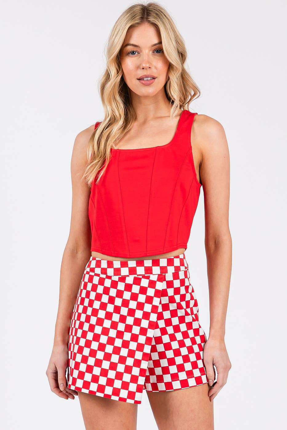 Woman wearing a red top and red and white checkered shorts on a white background