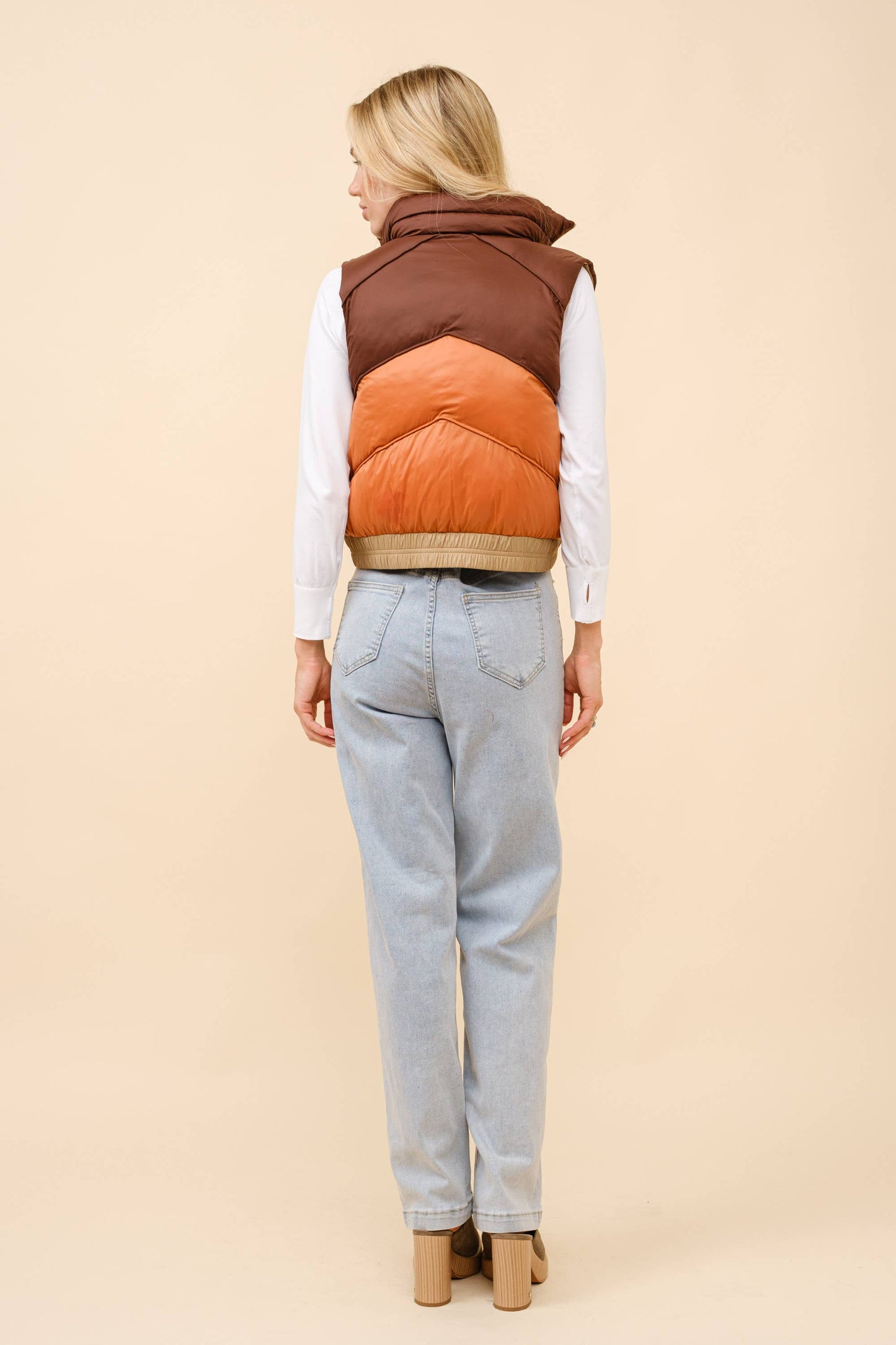 Person wearing a two-tone brown and orange vest on a beige background