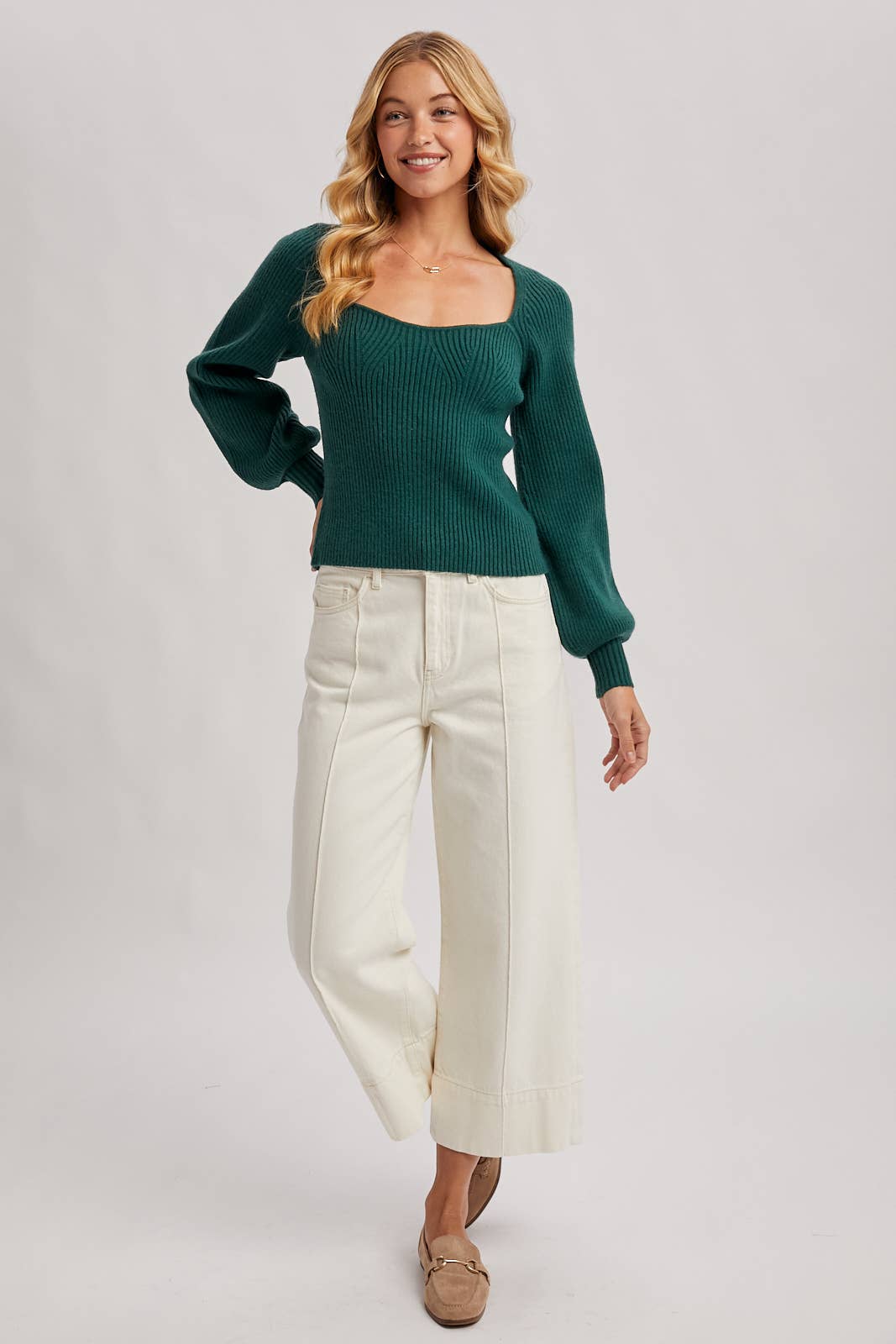 Woman wearing a green sweater and white pants on a gray background