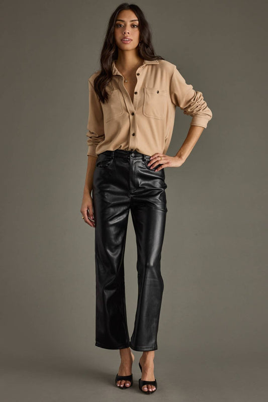Woman wearing a beige shirt and black leather pants against a gray background