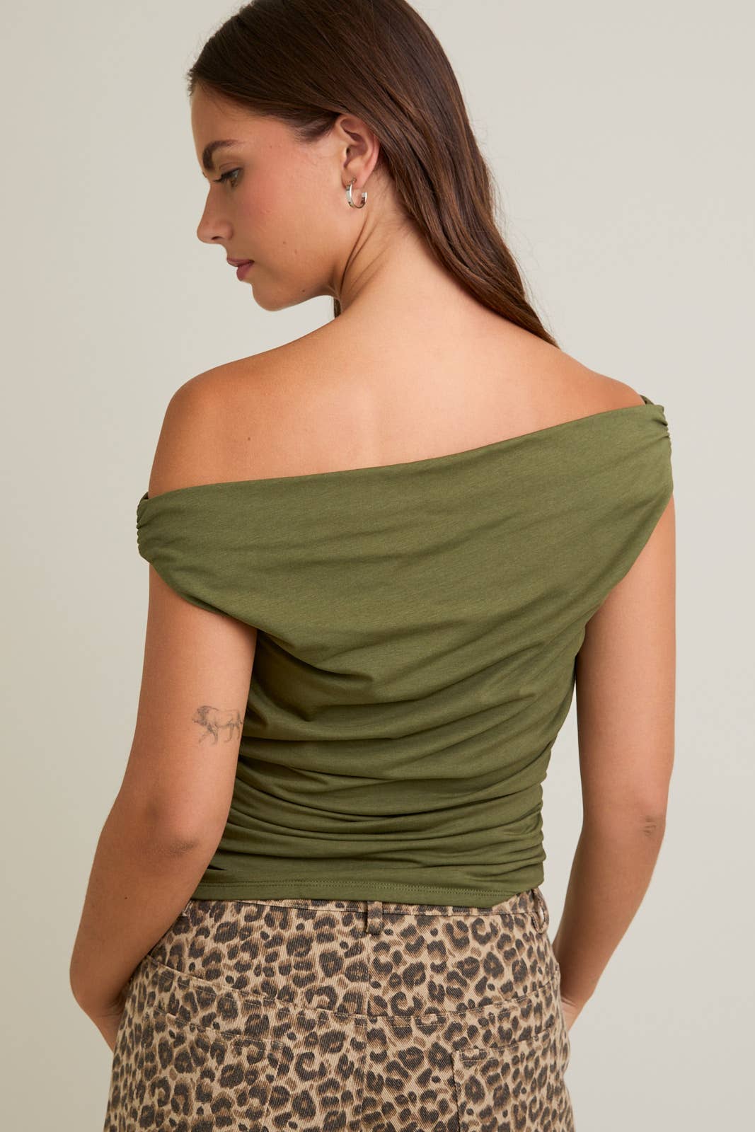 Woman wearing an off-shoulder green top with a leopard print skirt on a plain background