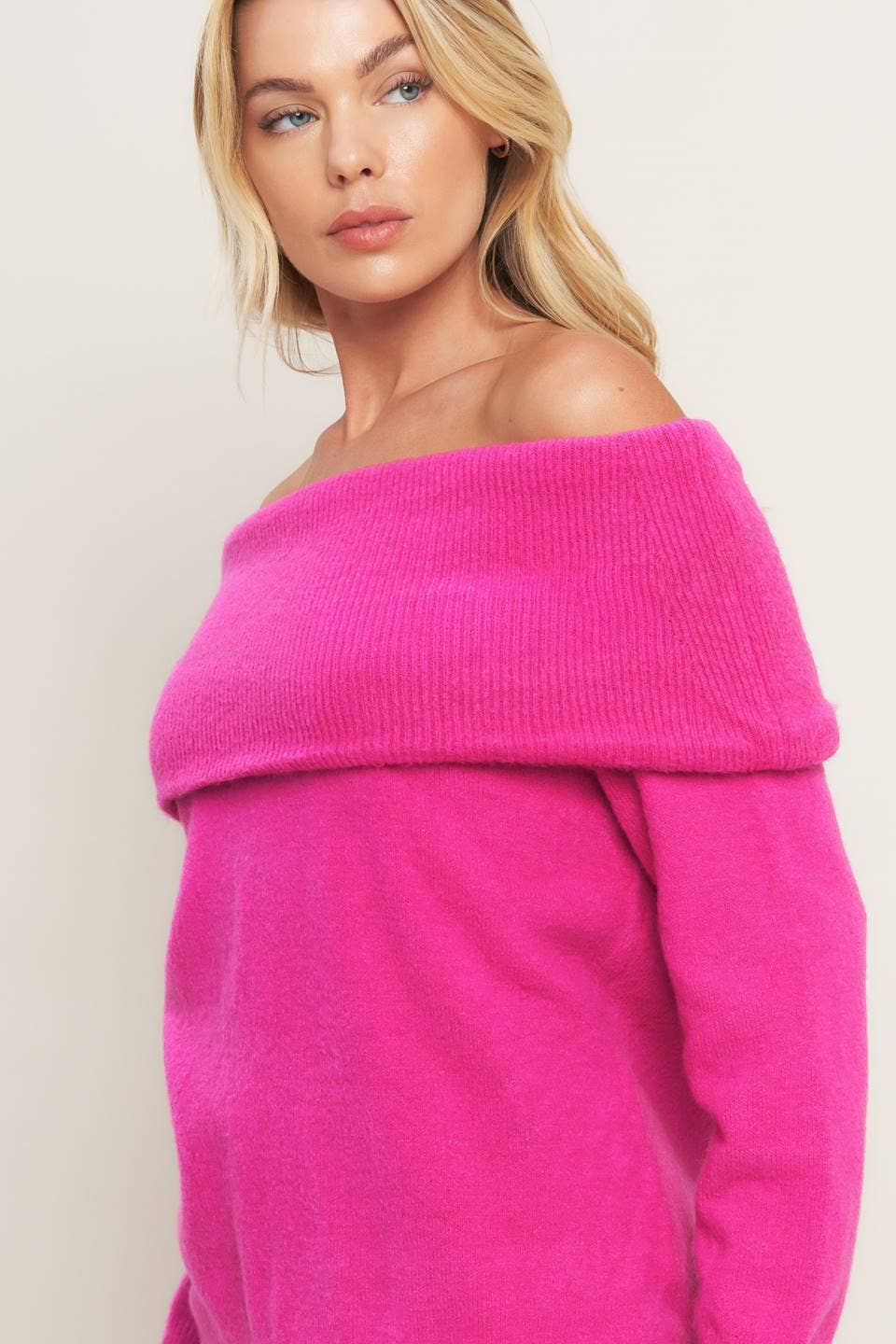 Woman wearing a bright pink off-shoulder sweater against a plain background