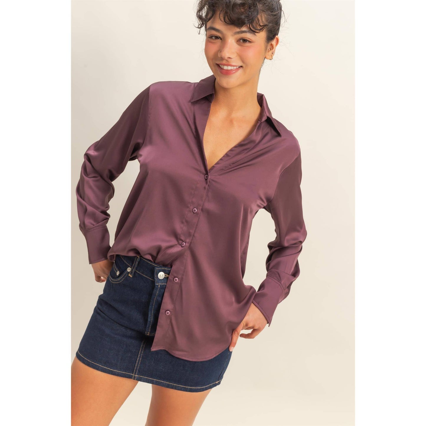 Woman wearing a long-sleeve purple shirt and denim skirt on a beige background