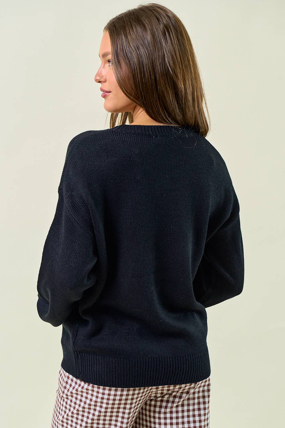 Woman wearing a navy sweater and checkered pants on a plain background