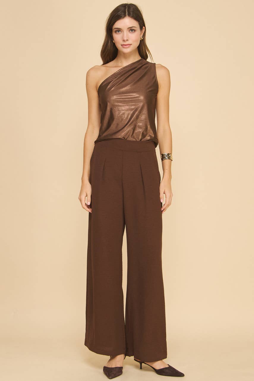 Woman wearing a brown one-shoulder top and wide-leg pants against a beige background