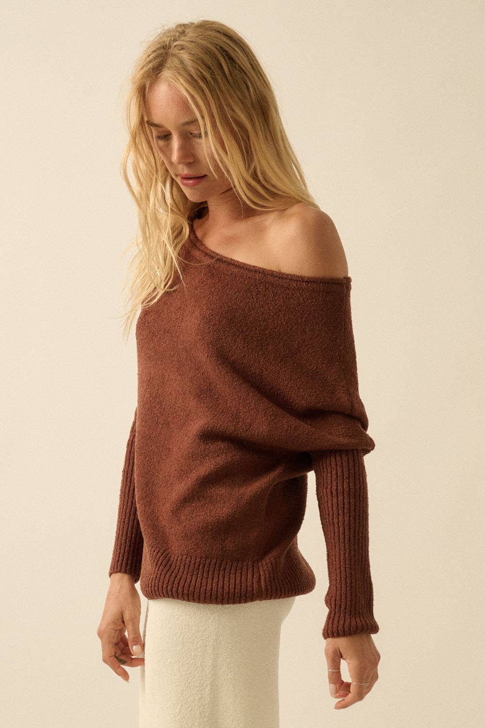 Woman wearing a brown off-shoulder sweater against a beige background