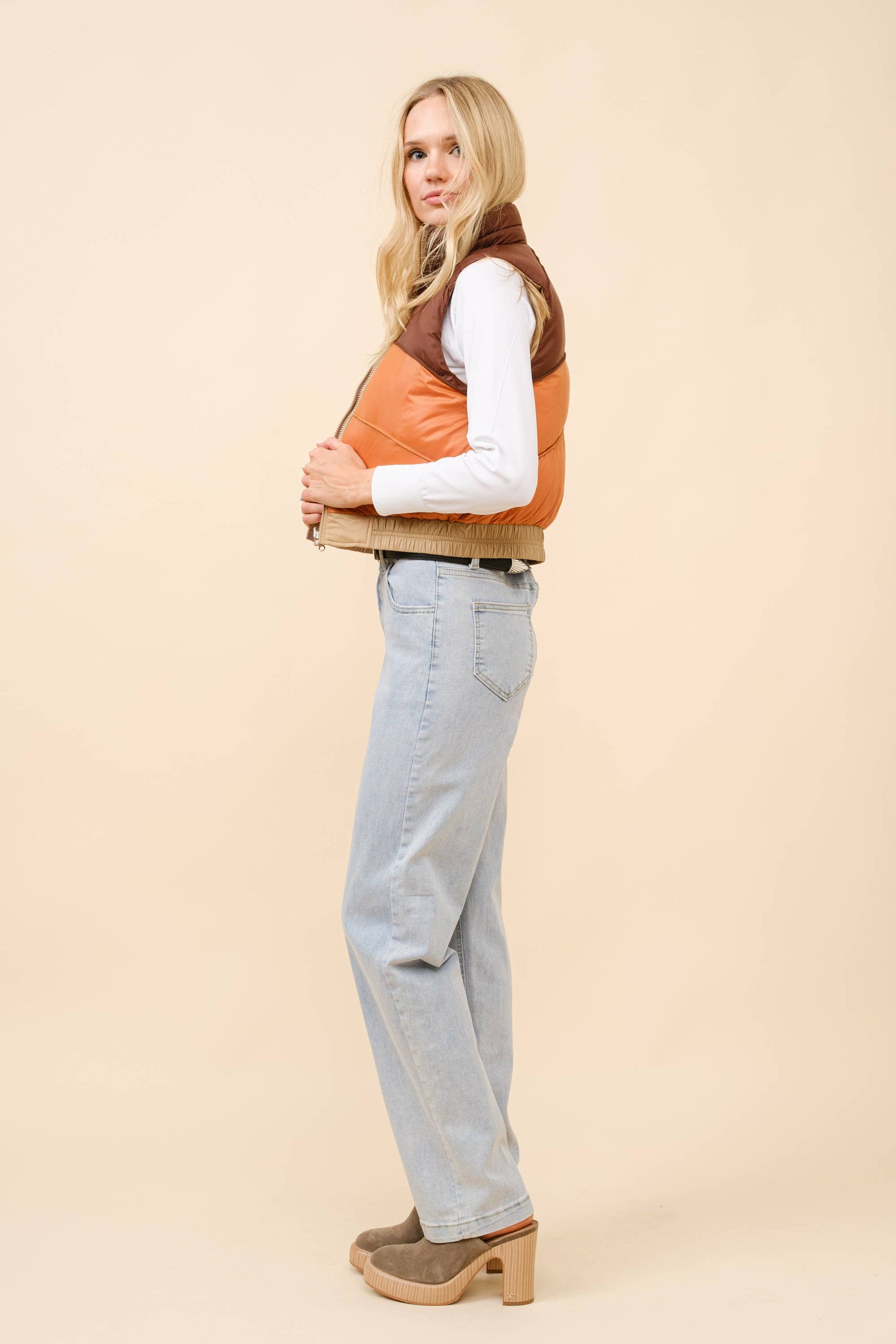 Woman wearing a two-tone vest and light blue jeans on a beige background