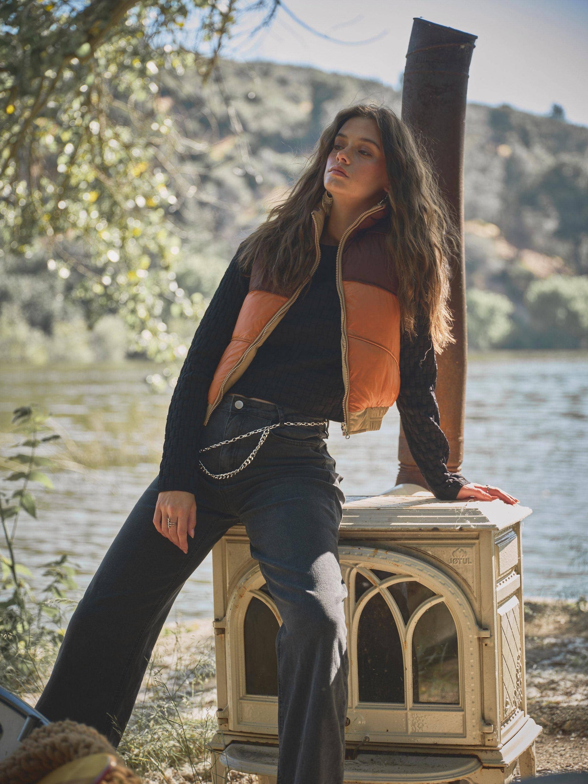 Woman posing outdoors by a lake with mountains in the background