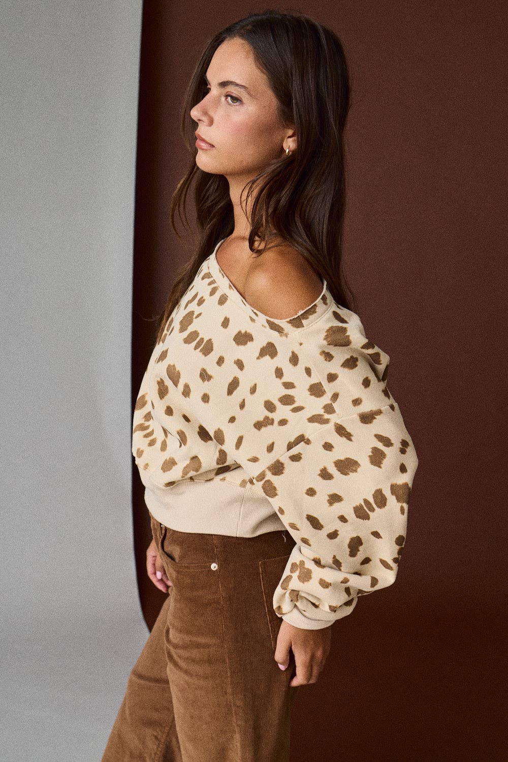 Woman wearing a beige blouse with brown leopard print and brown pants against a gradient background