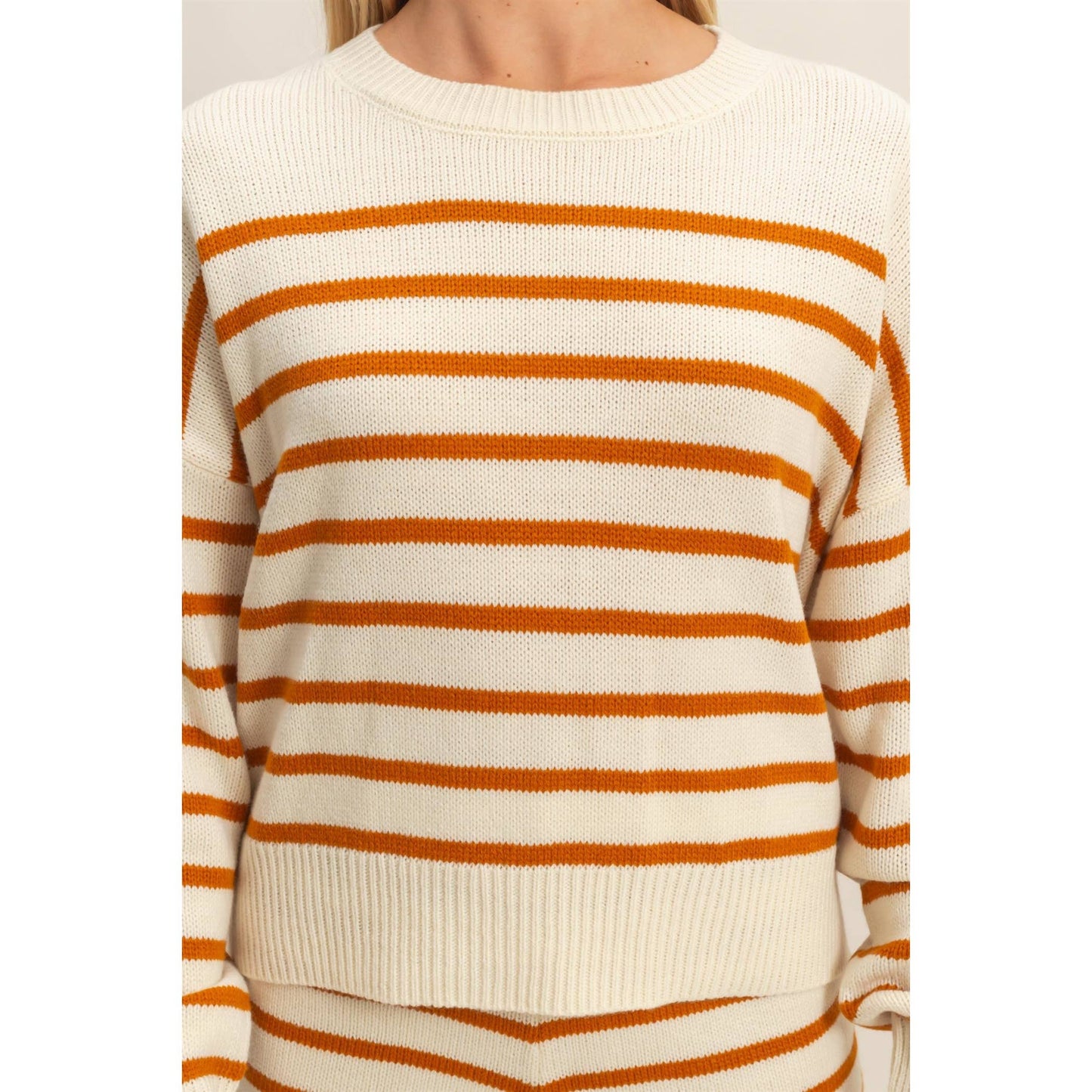 Close-up of a person wearing a cream and orange striped sweater on a white background