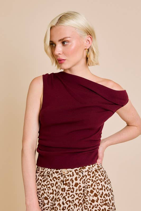 Woman wearing a burgundy one-shoulder top and leopard print pants on a beige background