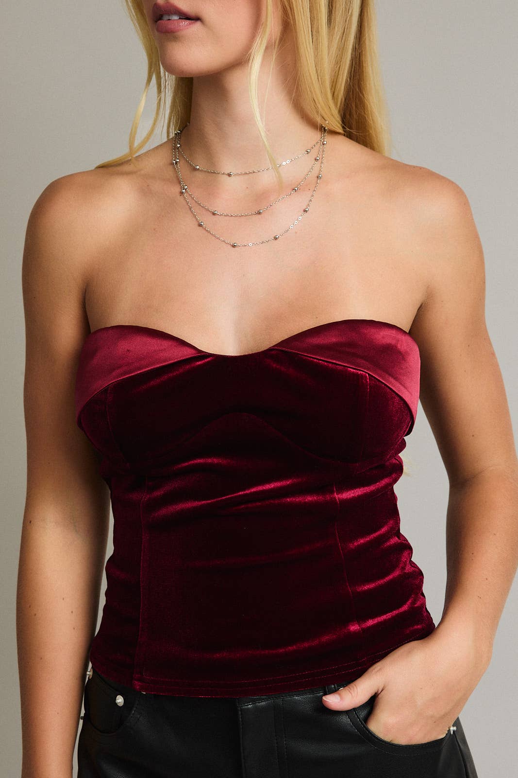 Woman wearing a strapless burgundy velvet top against a neutral background