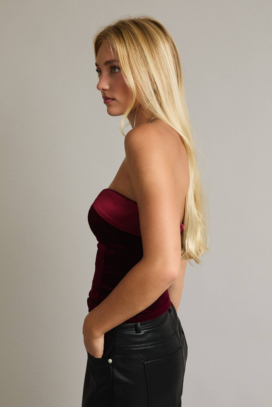 Woman wearing a strapless red top and black pants against a plain background