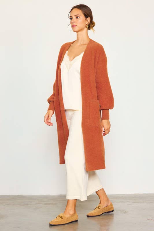 Woman wearing a rust-colored cardigan over a white outfit on a plain background