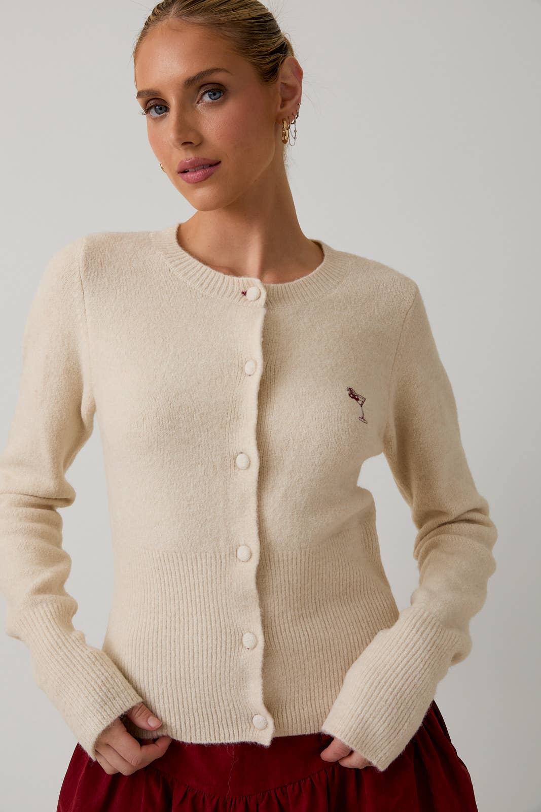 Woman wearing a beige cardigan with a small logo on a plain background