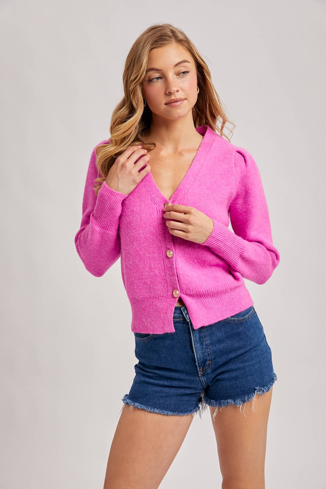 Woman wearing a pink cardigan and denim shorts on a plain background
