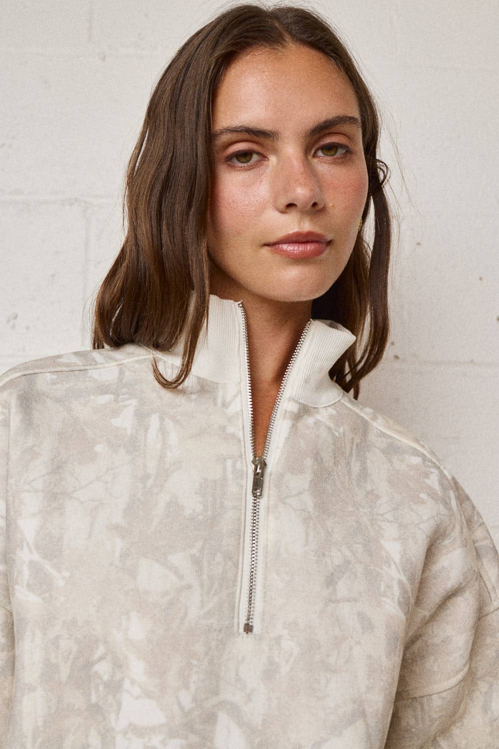 Woman wearing a light-colored pullover with a zipper against a white background