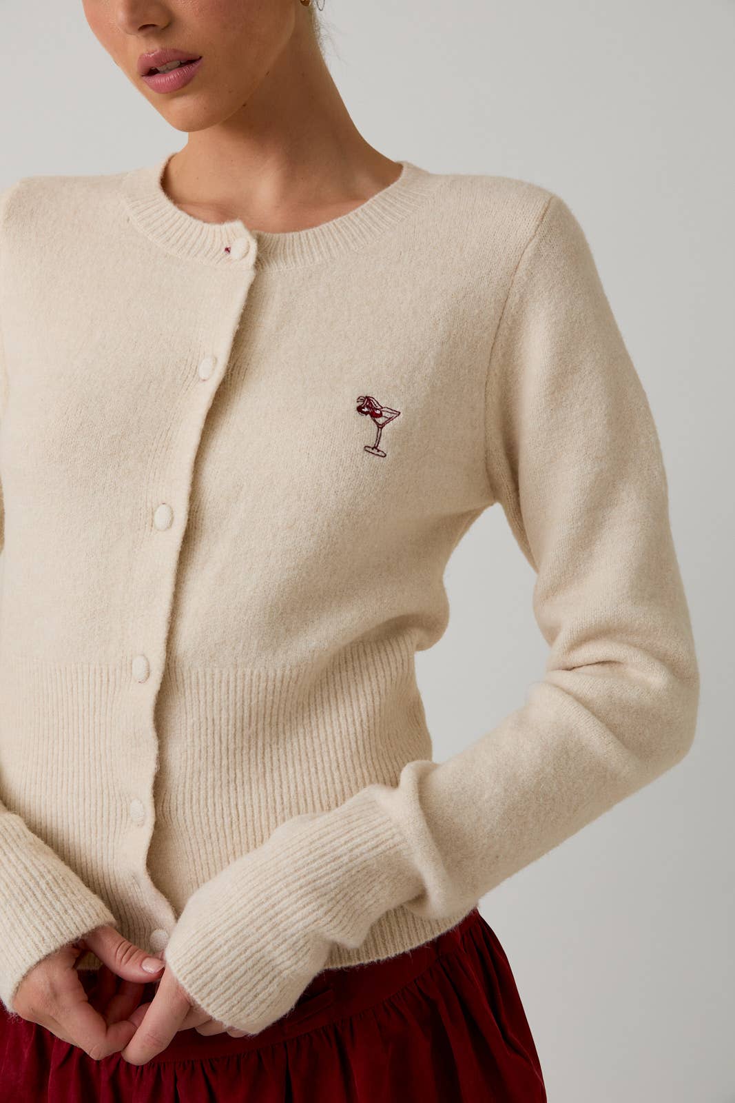 Beige cardigan with a small red and black design on a neutral background