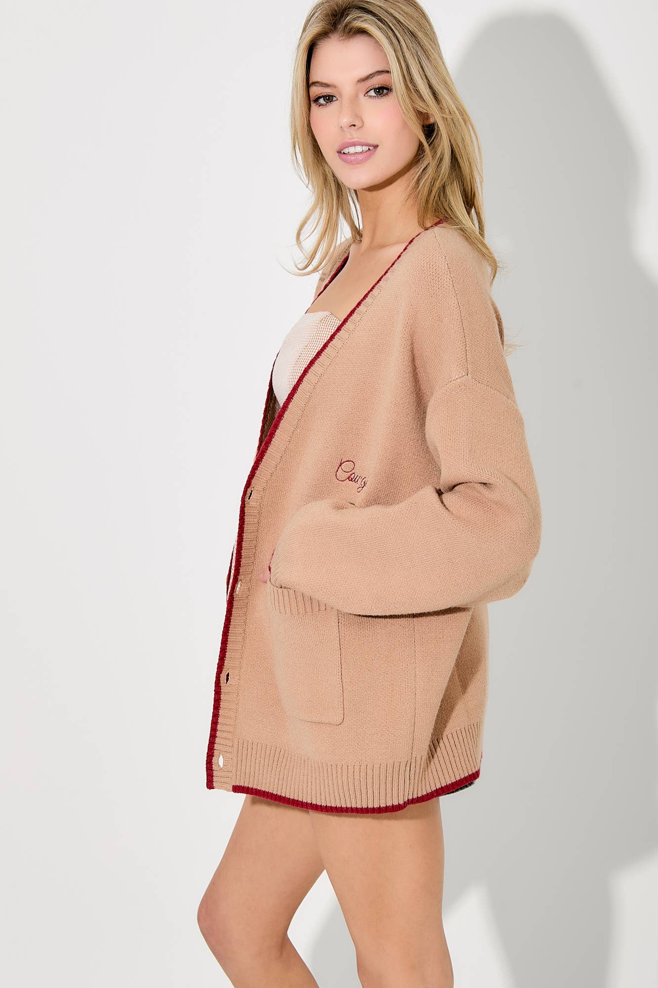 Woman wearing a beige cardigan with red trim on a white background