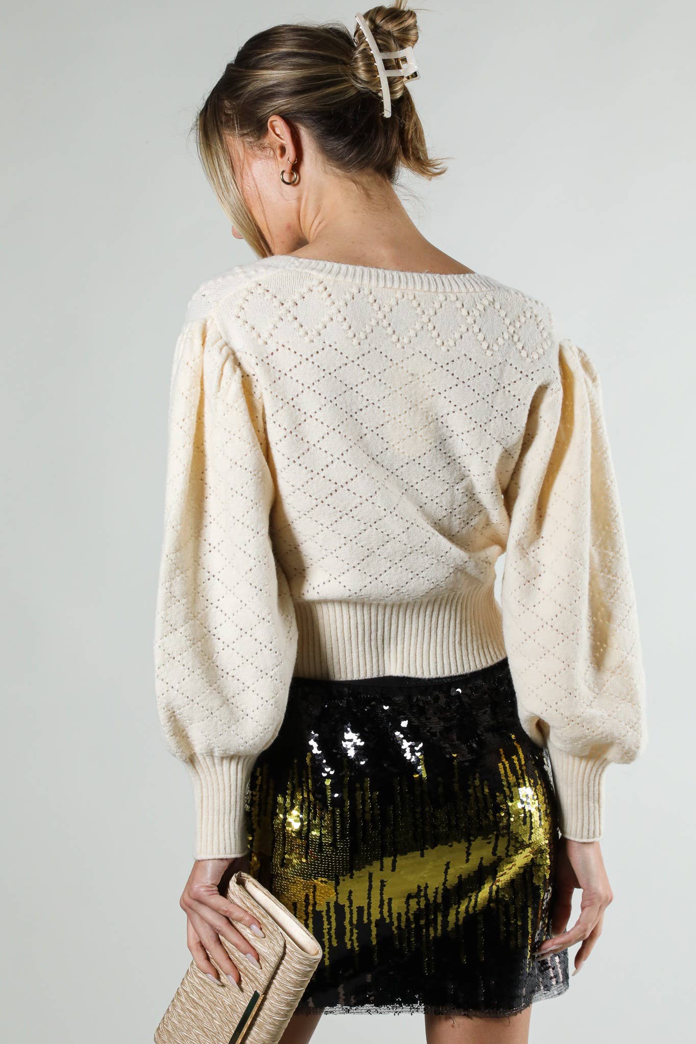 Woman wearing a cream sweater and black sequin skirt on a plain background