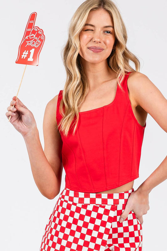 Woman wearing a red sleeveless top and red and white checkered pants, holding a foam finger with the number 1.
