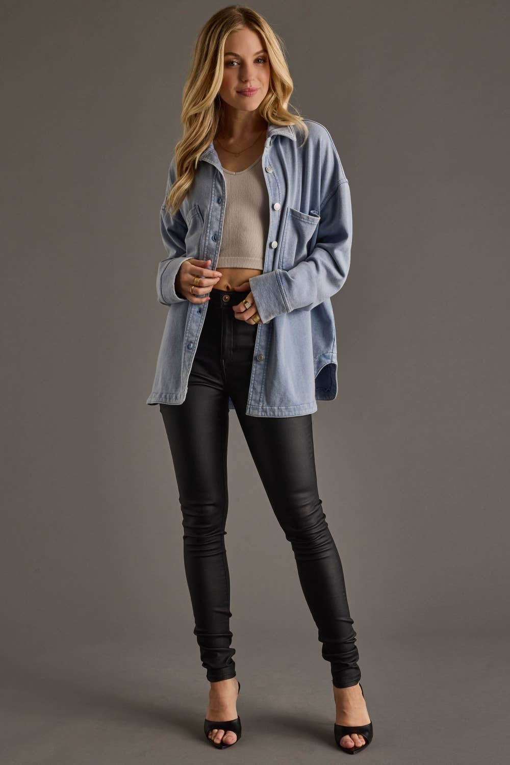Woman wearing a light blue denim jacket, beige top, black pants, and black high heels on a gray background