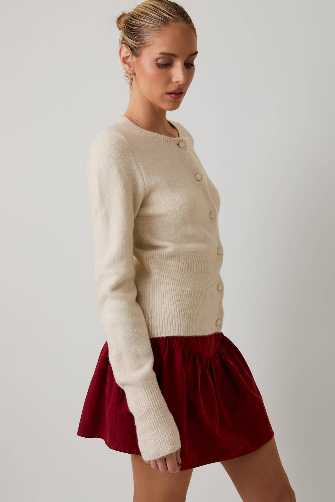 Woman wearing a beige cardigan and red skirt on a plain background