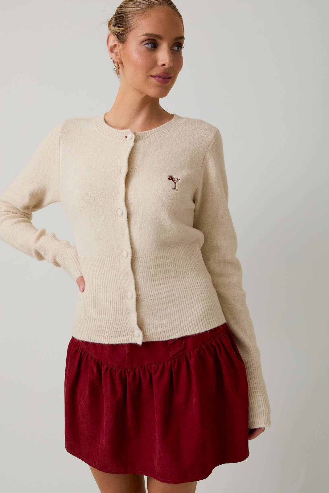 Woman wearing a beige cardigan with a small logo and a red skirt on a plain background