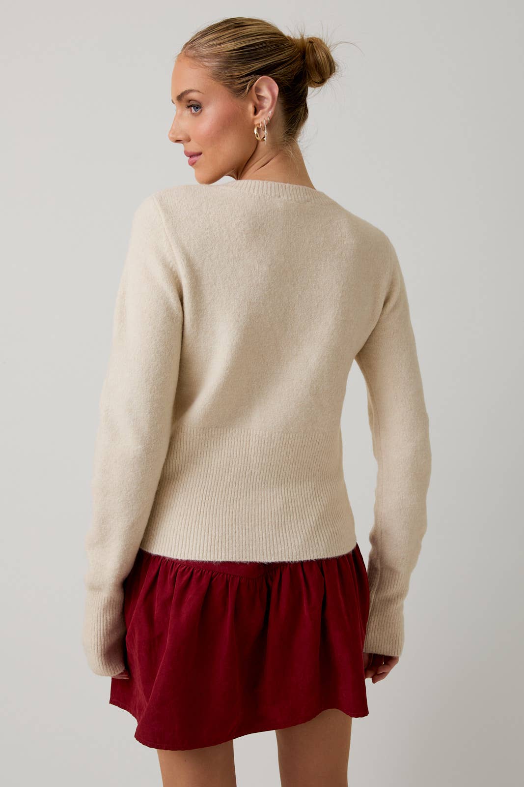 Woman wearing a beige sweater and red skirt on a plain background