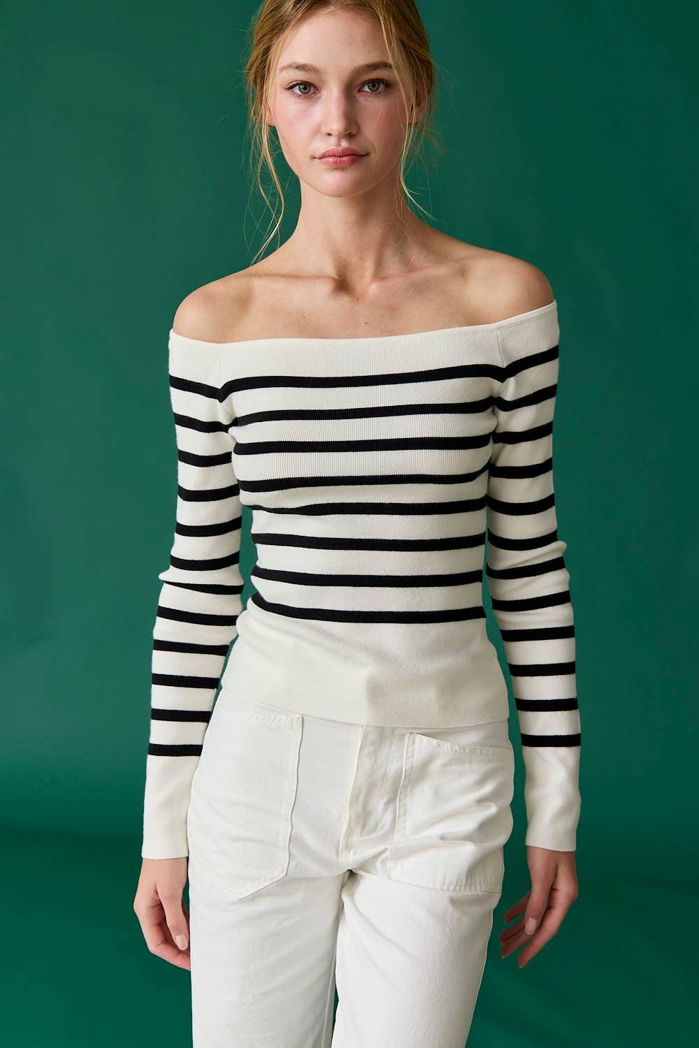 Woman wearing a black and white striped off-shoulder top with white pants against a green background
