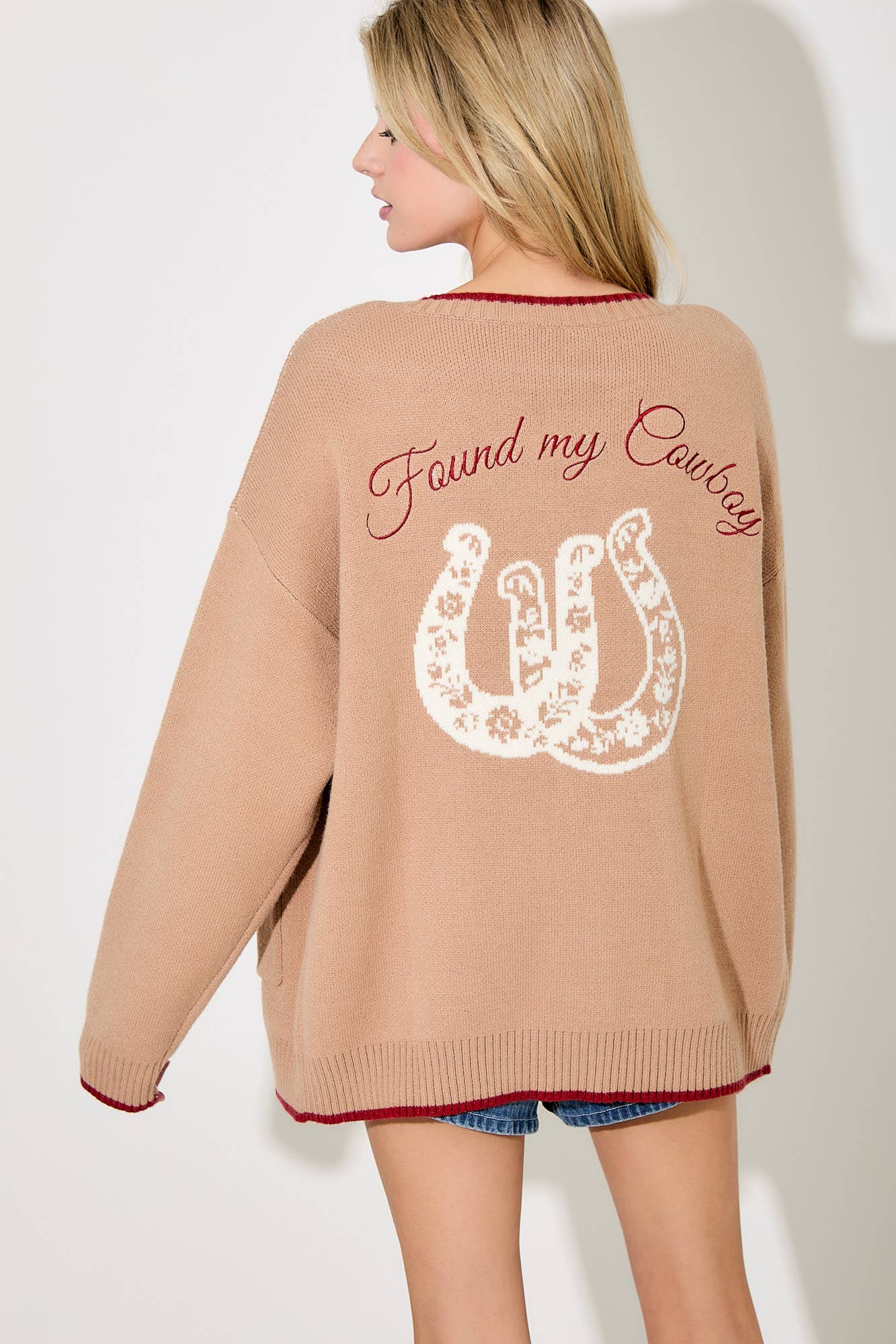 Woman wearing a beige cardigan with 'Found my cowboy' text and horseshoe design on the back.
