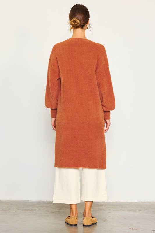 Person wearing a long rust-colored cardigan over a white outfit on a plain background