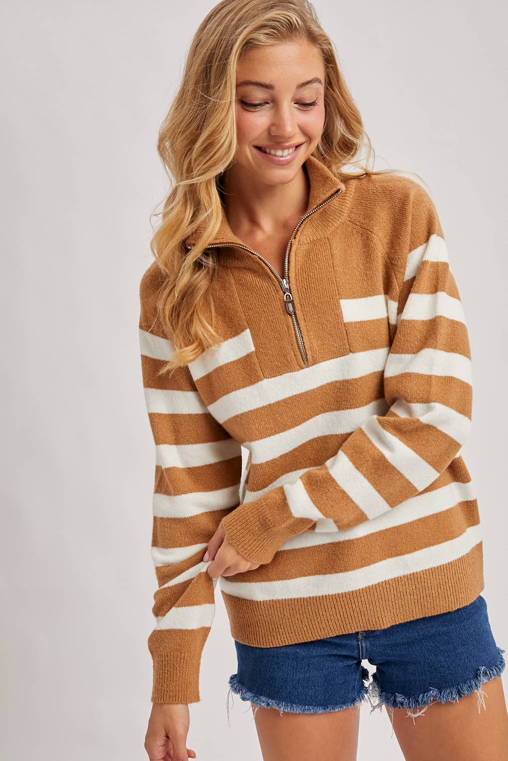 Woman wearing a striped brown and white sweater with blue shorts on a plain background