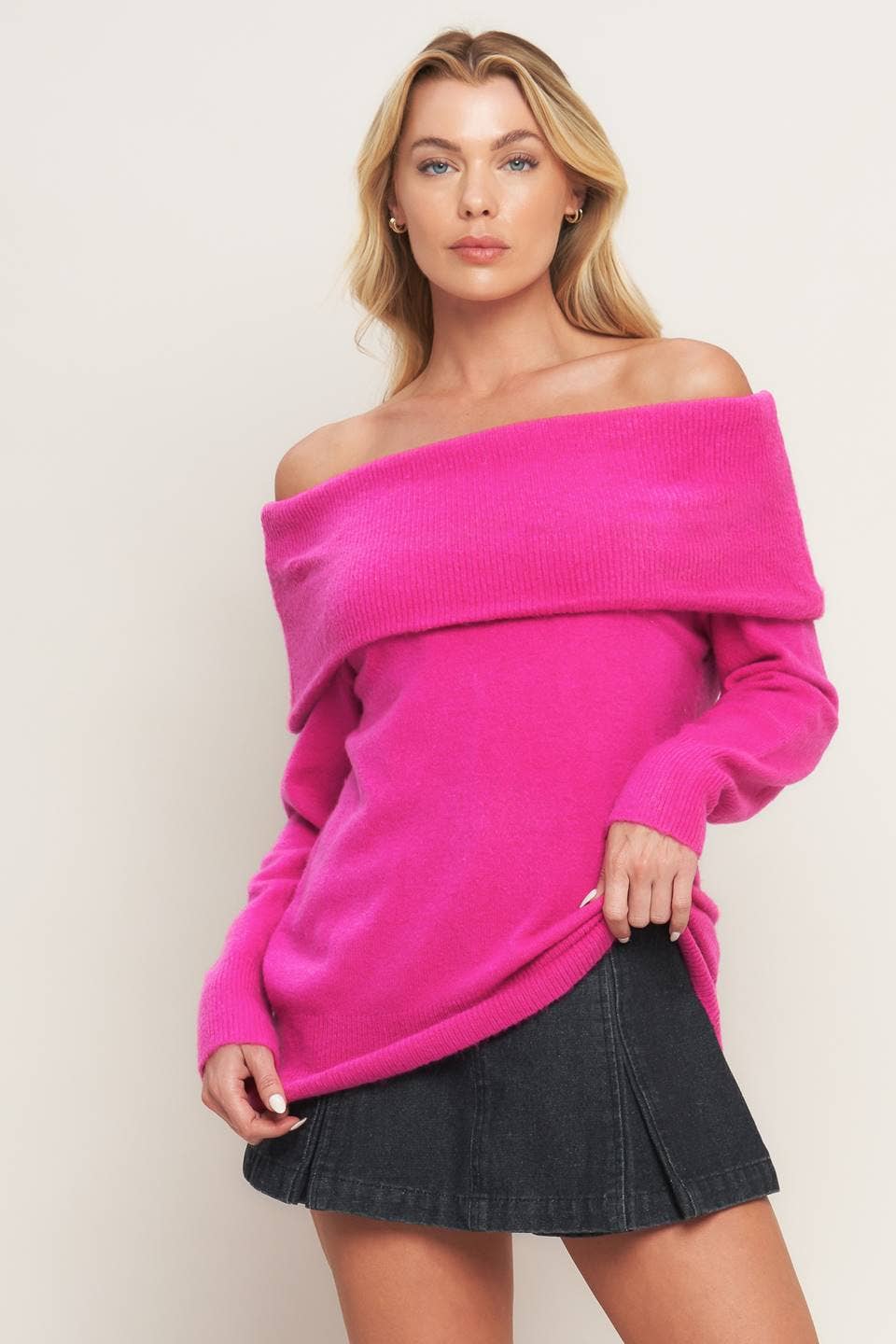 Woman wearing a bright pink off-shoulder sweater and black skirt against a plain background