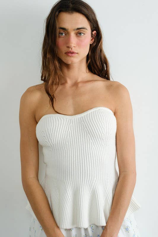 Woman wearing a white strapless top against a plain background