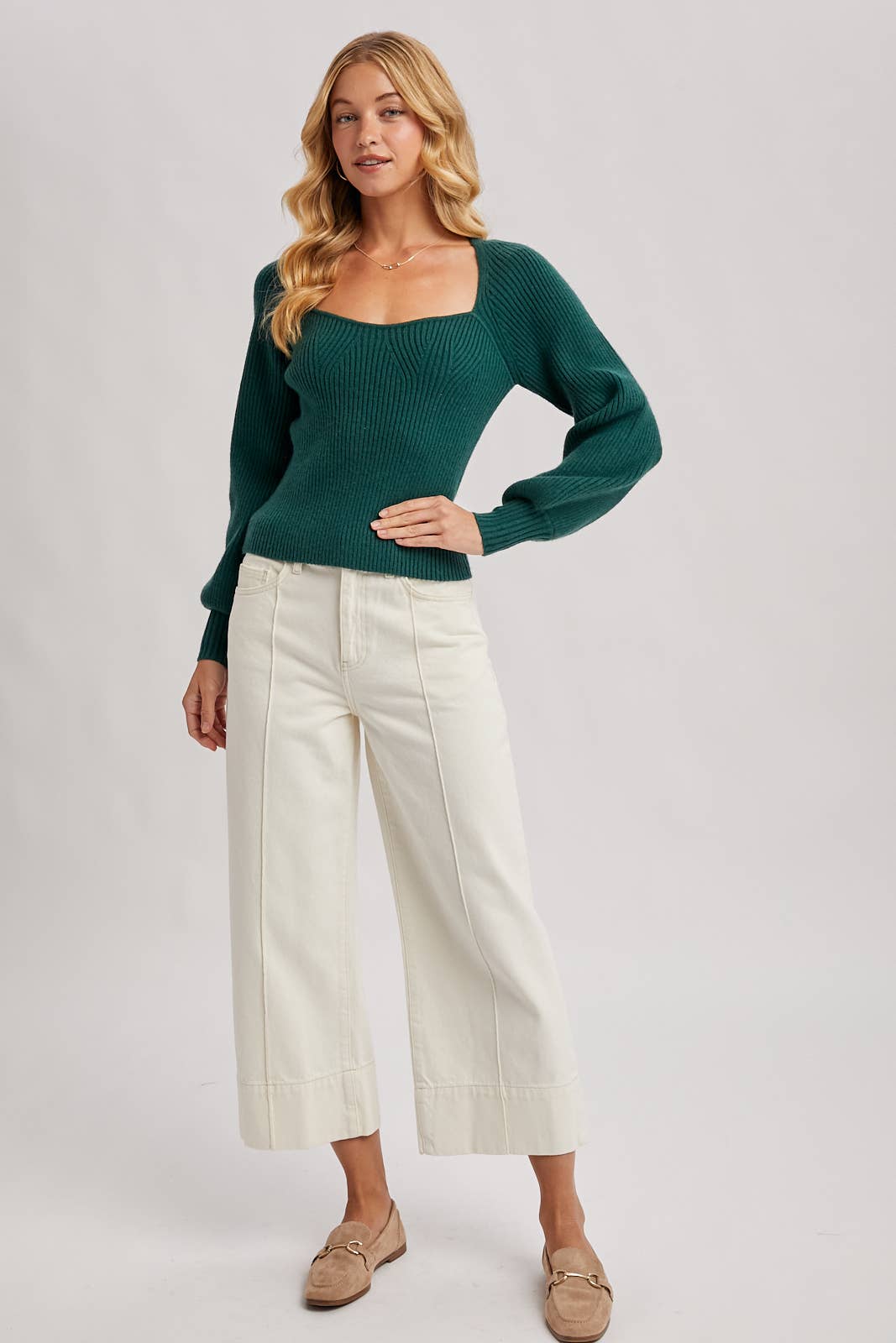Woman wearing a green sweater and white pants on a plain background