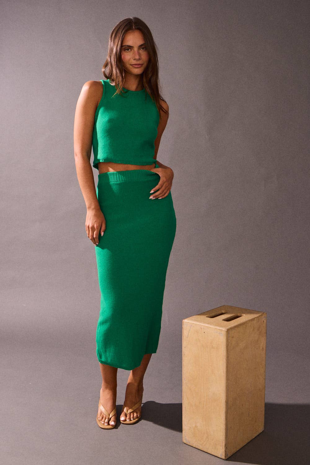 Woman in a green outfit standing next to a wooden block against a gray background