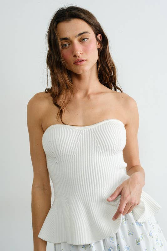 Woman wearing a white strapless top against a plain background