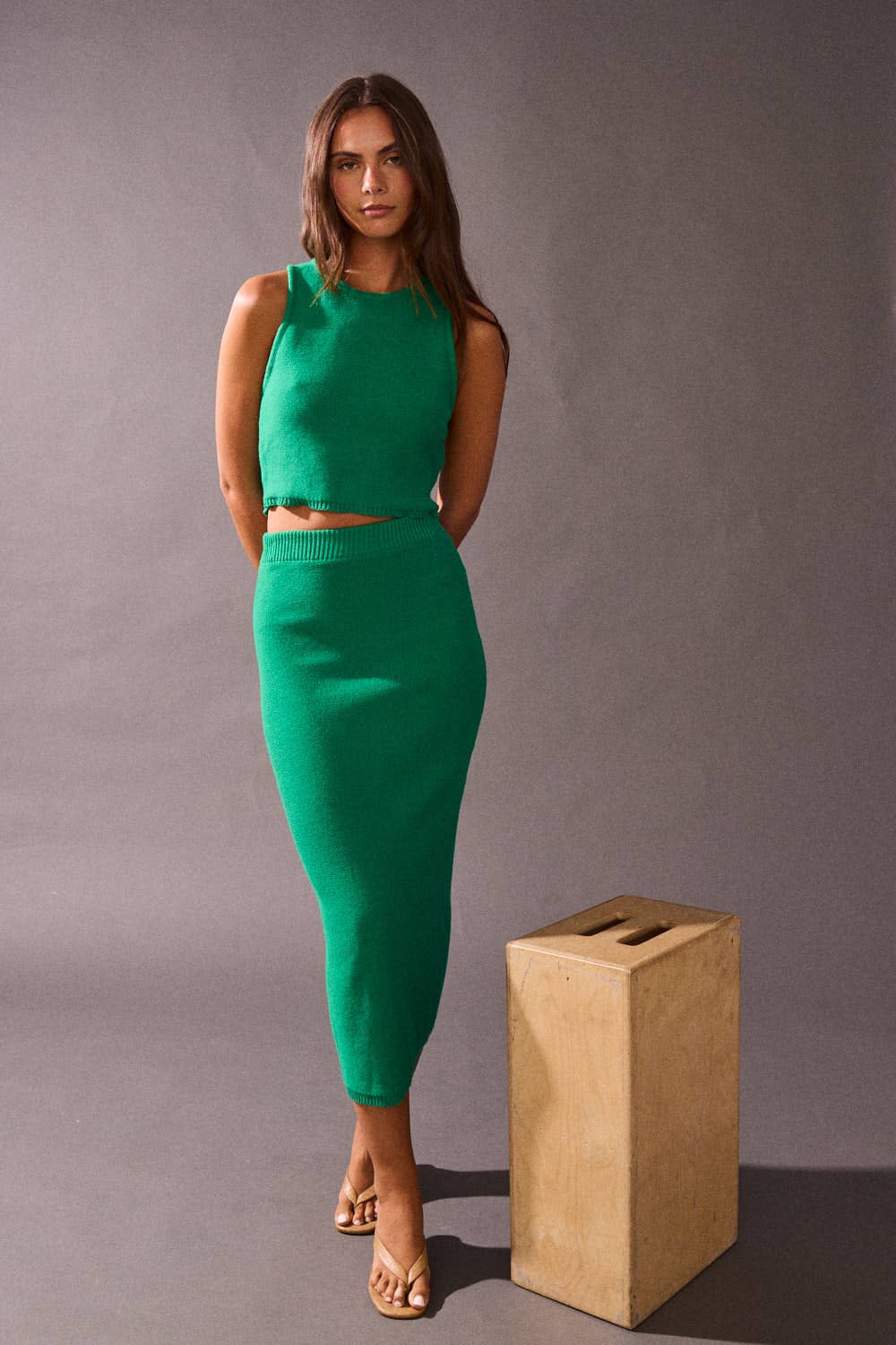Woman in a green dress standing next to a wooden box against a gray background