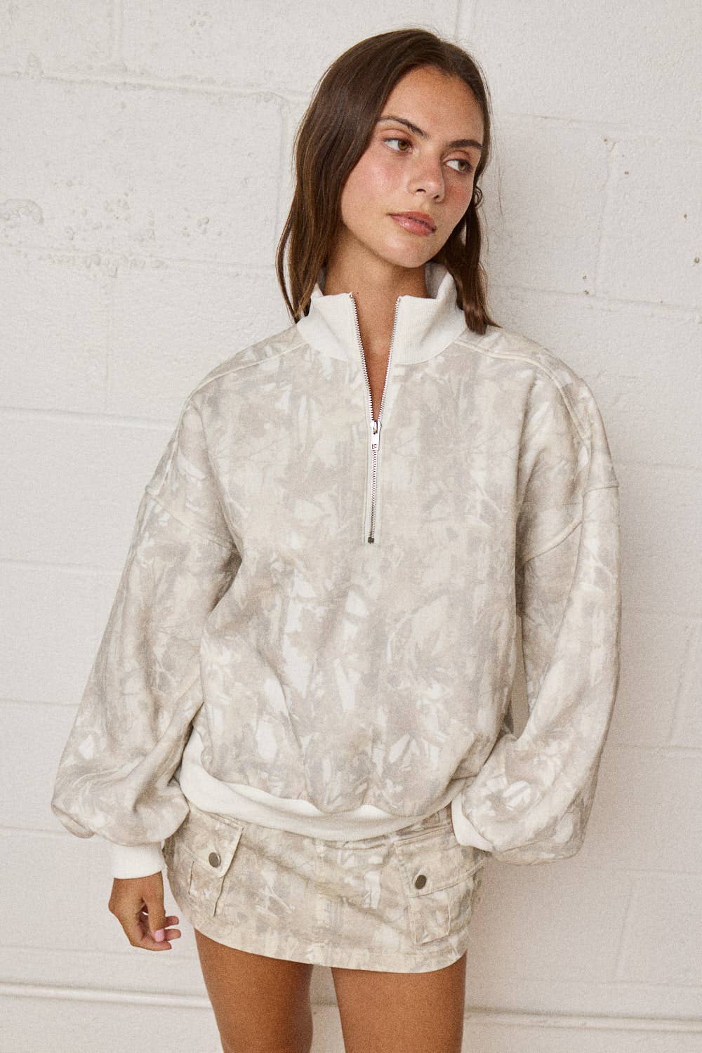 Woman wearing a patterned beige jacket and shorts against a white brick wall.