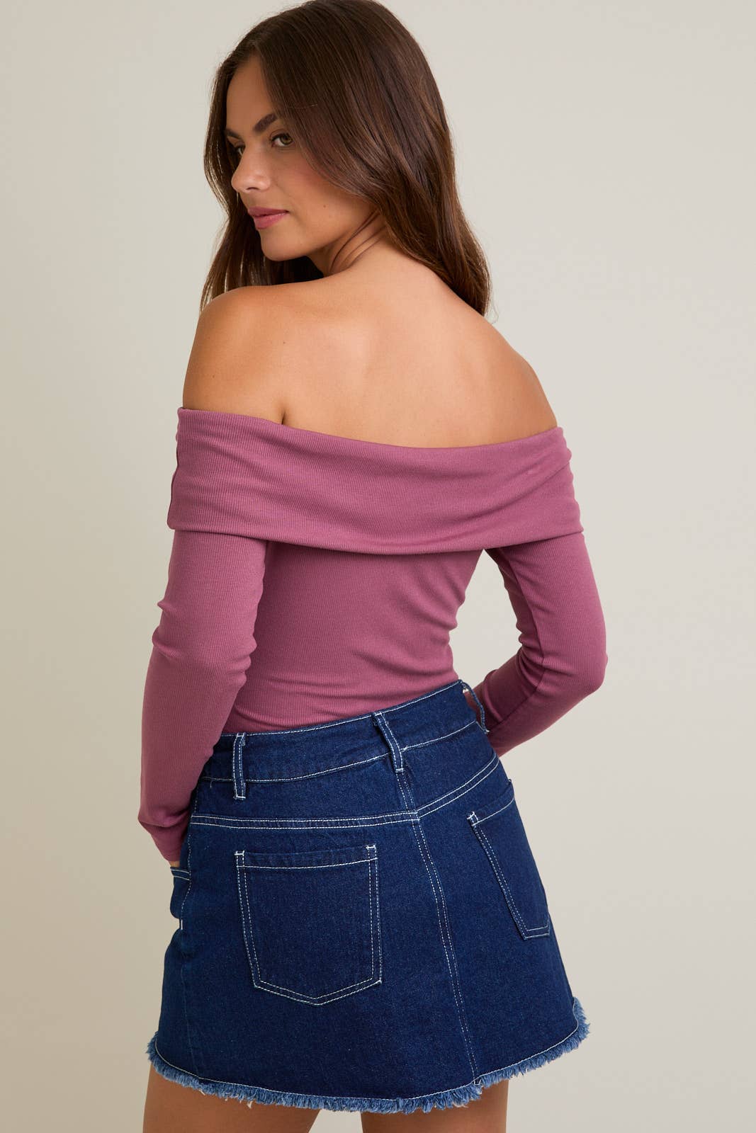 Woman wearing a pink off-shoulder top and blue denim skirt on a plain background