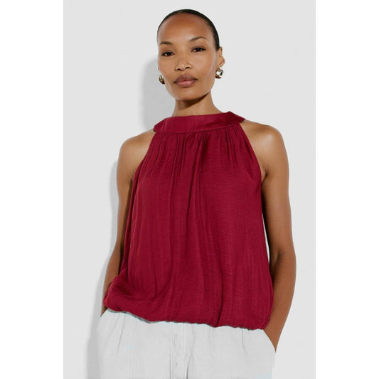 Woman wearing a red sleeveless top and white pants on a light gray background