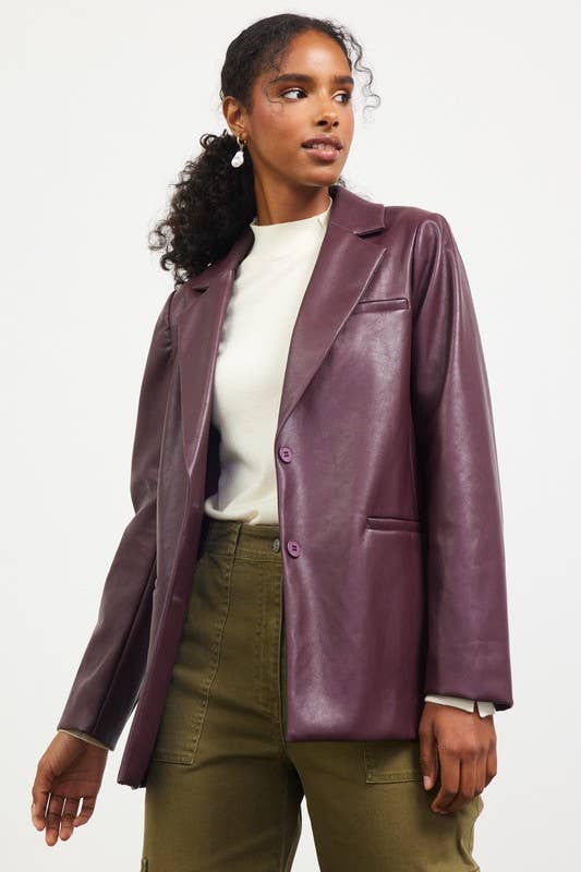 Woman wearing a purple leather jacket over a white shirt and green pants on a white background