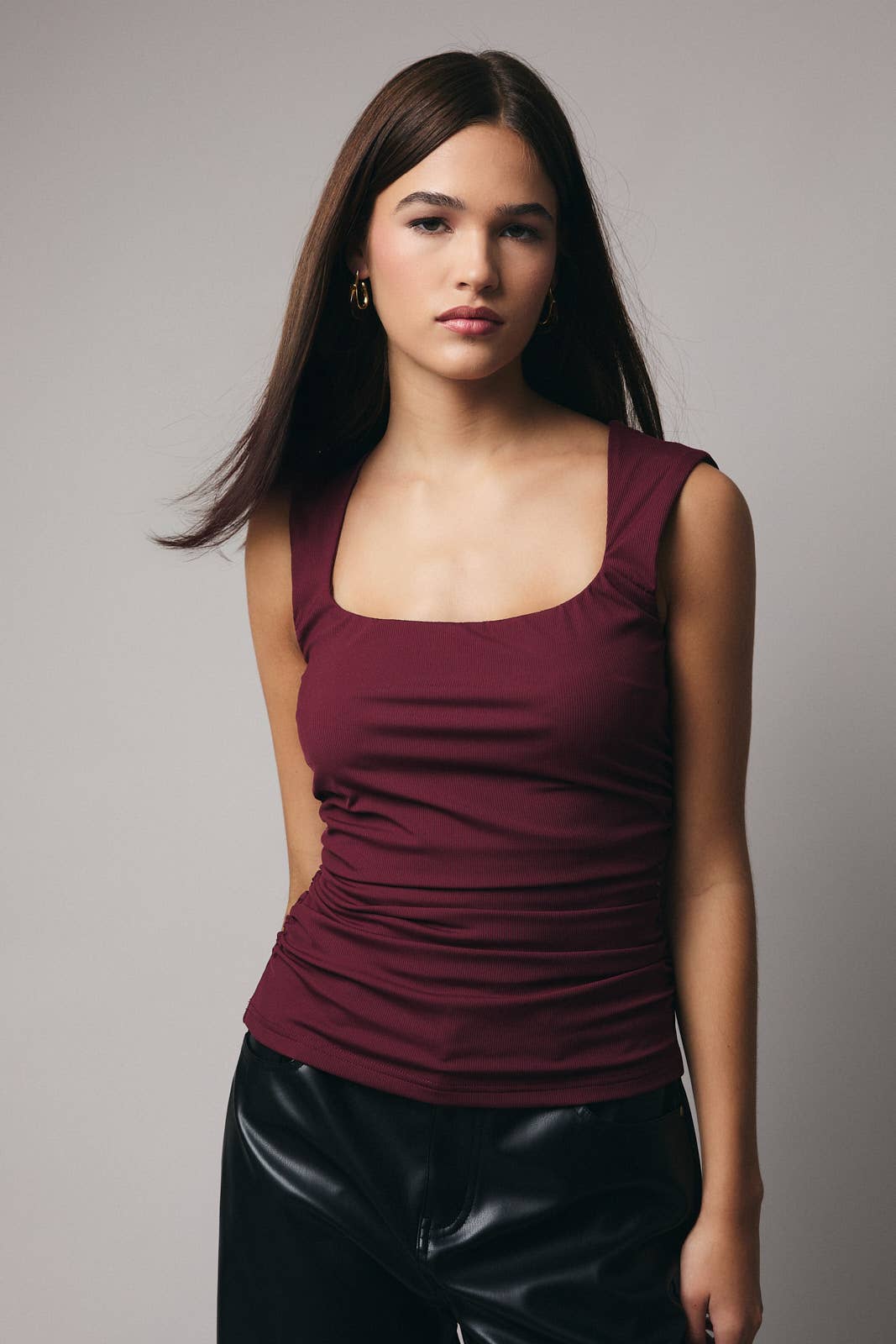 Woman wearing a maroon top and black pants against a gray background