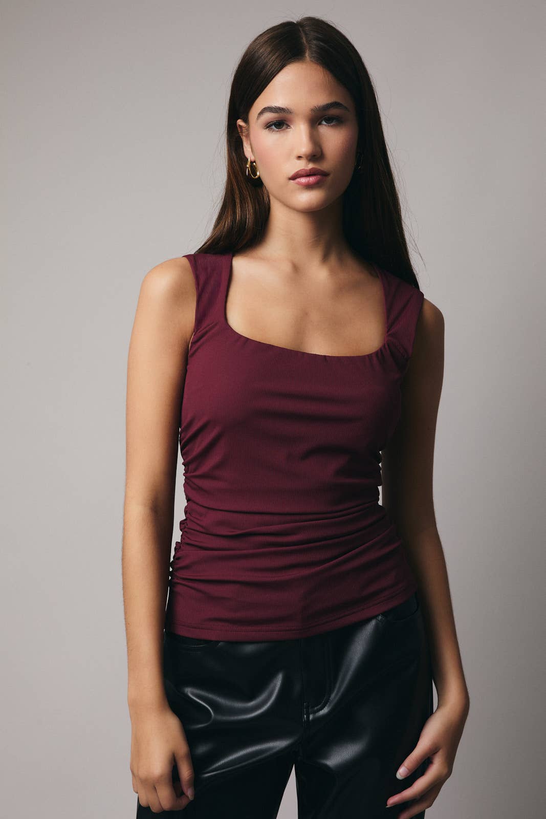 Woman wearing a maroon tank top and black pants against a gray background