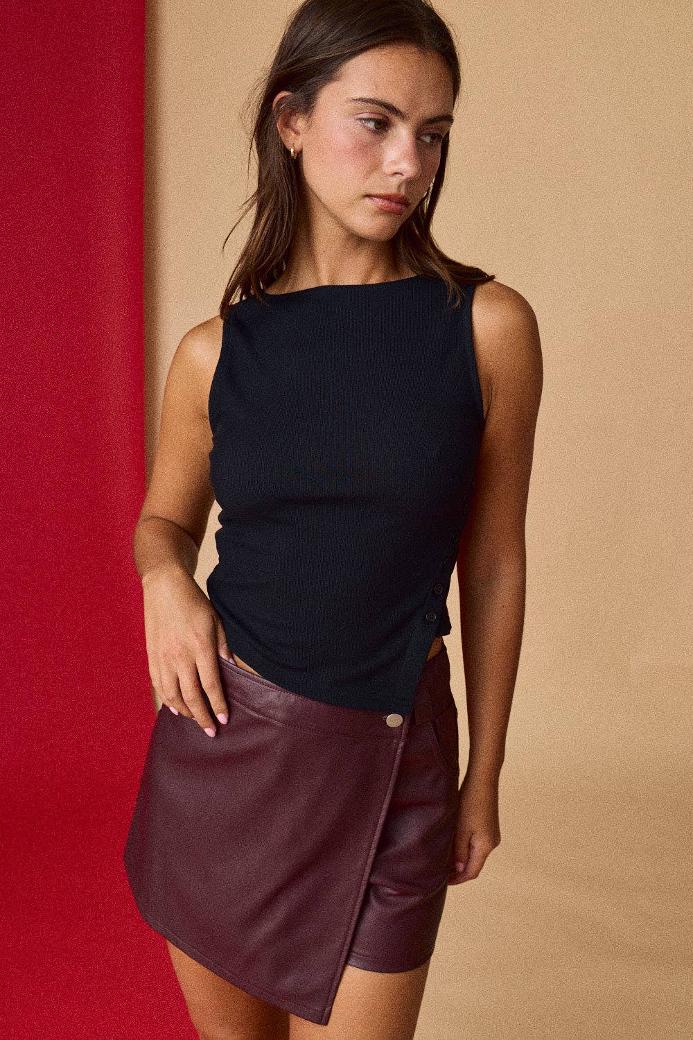Woman wearing a black top and maroon leather skirt against a red and beige background