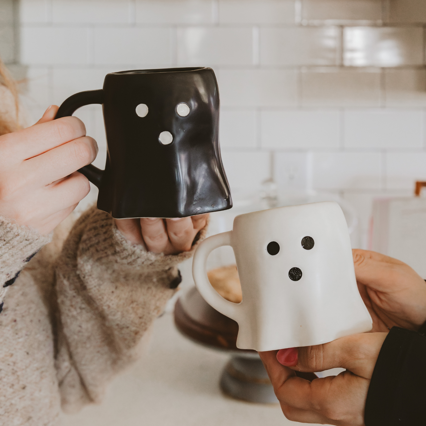 Two people holding black and white mugs with smiley face designs in a kitchen setting.
